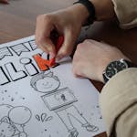 Photo by Nisa Eser Person coloring a creative drawing on paper with red pencil indoors.