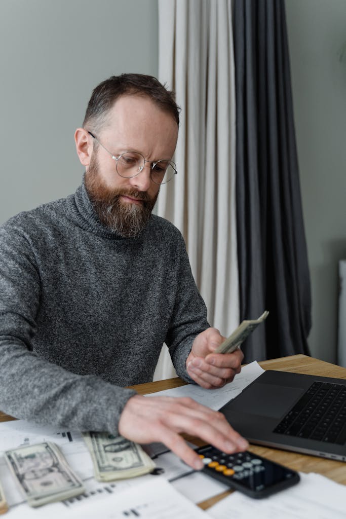 Businessman managing finances using calculator and cash indoors